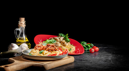 Heaped plate of delicious Italian spaghetti pasta with fresh basil leaves and grated parmesan cheese on dark background