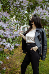 Girl in a medical mask on a background of blooming lilacs. Black mask. Protection against virus, flu. Coronavirus protection. epidemic of coronavirus. the aroma a tree in the garden Spring allergy