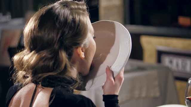 A young girl licks a plate in a restaurant