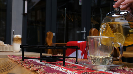 A female hand pours tea from glass teapot from birch chaga mushrooms. Organic drink antioxidant gray natural background.
