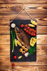 A slate plate from natural stone with a ready meal hangs on a wooden wall. For the menu. Grilled fish with vegetables, mushrooms and herbs. Selective focus.