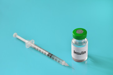 Medical vial of insulin and a disposable syringe on a turquoise background, selective focus. Healthcare concept.