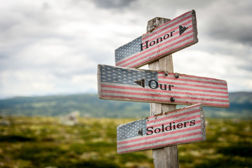 honor our soldiers text on wooden american flag signpost outdoors in nature.