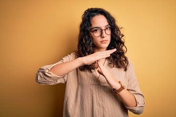 Beautiful woman with curly hair wearing striped shirt and glasses over yellow background Doing time...