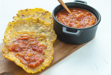 Fried banana with fried tomato in a black pot on a white board. Typical dish of Colombian cuisine. Copy space. Patacón con hogao.