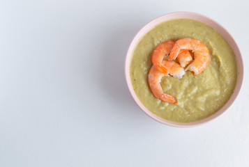 broccoli soup with king prawns in a pink bowl on a white background