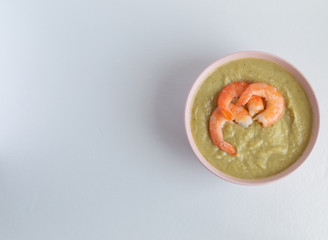 broccoli soup with king prawns in a pink bowl on a white background
