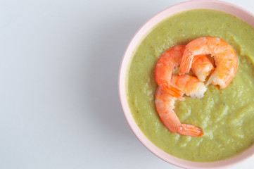 broccoli soup with king prawns in a pink bowl on a white background