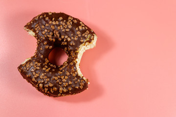 Bitten tasty chocolate donut on a pink background. Top view