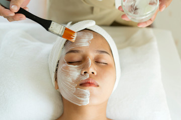 Schöne junge asiatische Frau, die Gesichtspflege von Kosmetikerin im Spa-Salon bekommt, Gesichtspeeling-Maske, Spa-Schönheitsbehandlung, Hautpflegekonzept