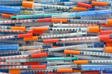 Many different close-up disposable insulin syringes arranged horizontally as a background, top view. Healthcare concept.