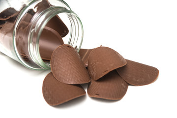 Closeup of chocolate in shaped tiles falling from a glass container on white background