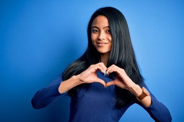 Young beautiful chinese woman wearing casual t-shirt over isolated blue background smiling in love showing heart symbol and shape with hands. Romantic concept.