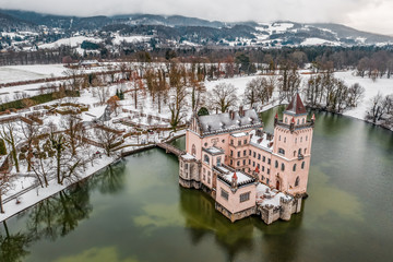 Aerial drone shot of Anif Schloss moated castle in artificial pond at Salzburg outskirts in heavy snow during winter time
