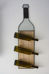 A wine bottle stand with three bottles hangs on a wall.