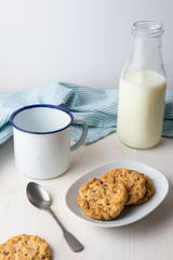 Top view of chocolate chip cookies, with plate, milk bottle, cup, spoon and dishcloth on white background, vertical