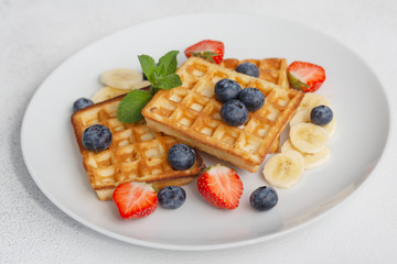 Delicious waffles with blueberries, strawberries and bananas. Plate with tasty waffles.
