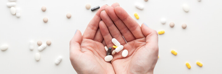 Colorful pills scattered on a white background. Hands with tablets. Panorama