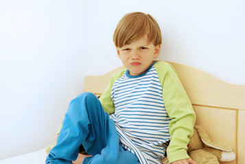 Ein vierjähriger Junge sitzt bockig auf seinem Bett