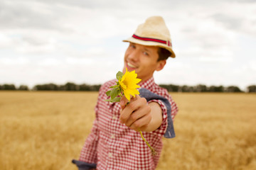 Young handsome happy man with sunflower in hands standing in wheat field 