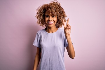 Young beautiful african american woman wearing casual t-shirt standing over pink background smiling with happy face winking at the camera doing victory sign. Number two.