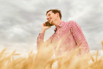 Young handsome happy man standing in wheat field talking by mobile