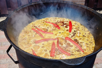 National Uzbek dish pilaf, pilaw, plov, rice with meat in big pan. Cooking process in a cauldron on fire. Preparation stage. pour out rice, Add waters, red pepper and the whole garlic