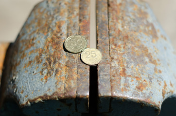 Ukrainian coins in denominations of 25 and 50 lie on an old iron vice. The concept of a crisis in the country.