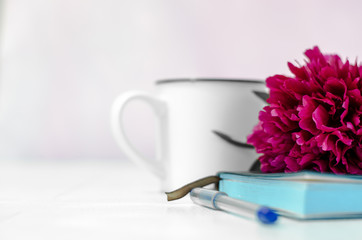 The flower lies on a notebook. Pen and notebook close-up. White cup in the background.