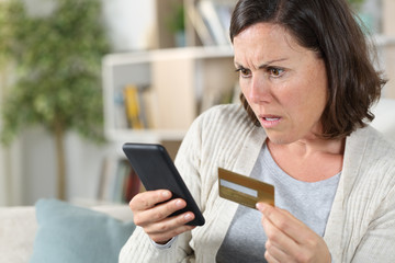 Worried adult woman paying on phone with card at home