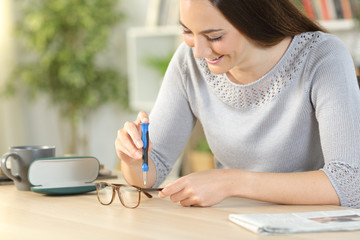 Woman fixing eyeglasses with screwdriver at home