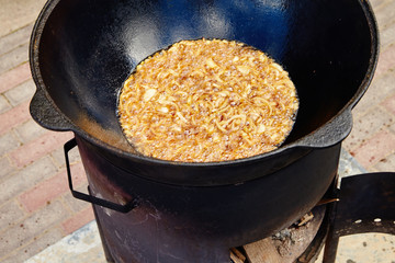 National Uzbek dish pilaf, pilaw, plov, rice with meat in big pan. Cooking process, open fire. Cooking in a cauldron on fire. .Preparation stages. Onions roasting to color of caramel, pilau