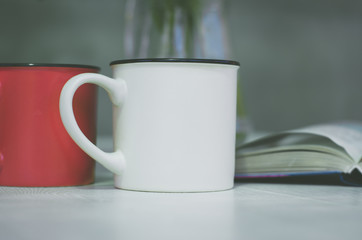 Two cups close up. In the background is a book and a vase of flowers. Cup with place for your text.