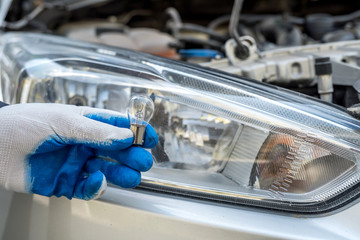 male's hand holding light bulb of car headlight for repair auto