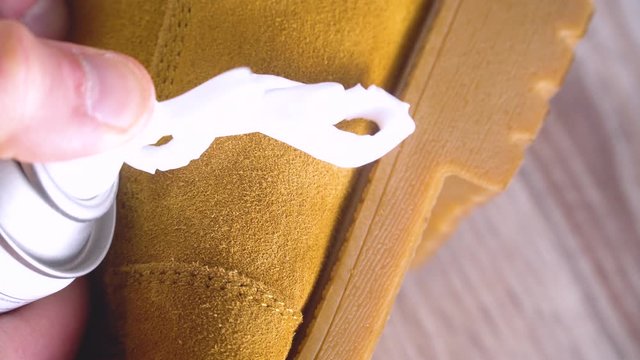 man's hand applies cleaning foam to a dirty brown nubuck or suede shoe and brushes it