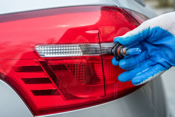 male's hand holding light bulb of car headlight for repair auto
