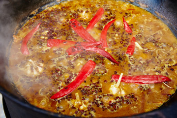 National Uzbek dish pilaf, pilaw, plov, rice with meat in big pan. Cooking process in a cauldron on fire. Preparation stage. pour out rice, Add waters, red pepper and the whole garlic
