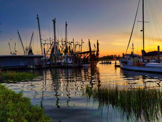 shrimping boats on creek with fishermen motoring by colorful sunset