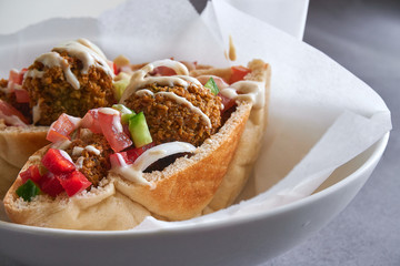 Authentic fresh falafels balls inside of two halves of pita bread sandwich with chopped salad and drizzle of tahini sauce on top, close-up of chickpea falafel in a gluten-free pita 