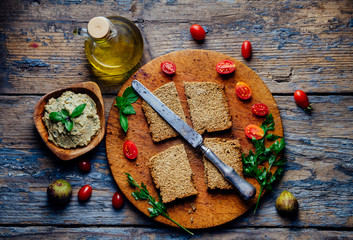 Top view of eggplant tahini dip, bread, cherry tomato and olive oil on vintage wooden table....