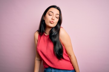 Young brunette woman wearing casual summer shirt over pink isolated background looking at the camera blowing a kiss on air being lovely and sexy. Love expression.