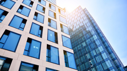 Bottom view of office building window close up with sunrise, reflection and perspective. Modern architecture with sun ray. Glass facade on a bright sunny day with sunbeams on the blue sky. 