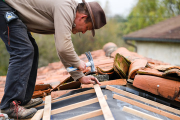 construction worker on a renovation roof covering it with tiles using hammer, crane and grinder