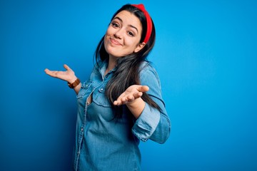 Young brunette woman wearing casual denim shirt over blue isolated background clueless and confused...