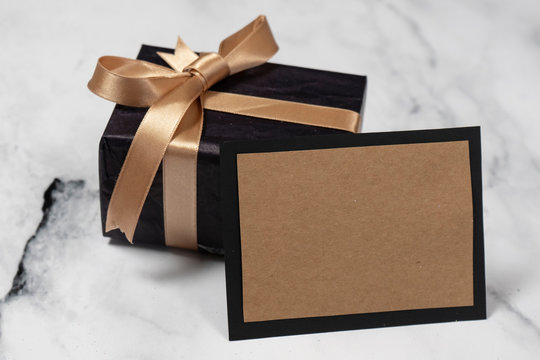 Black gift box with a golden ribbon With an empty Card on a white and black marble table.