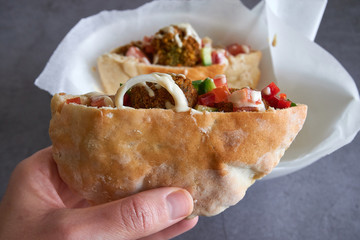 Woman hand hold an authentic half pita bread sandwich with fresh falafels balls inside and chopped salad and drizzle of tahini sauce on top, close-up of chickpea falafel in gluten-free pita