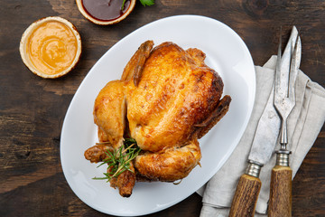 Whole Roasted Chicken on white plate with rosemary, sauces and vegetables