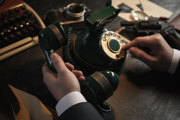 Detective dialing number on vintage telephone at table, closeup