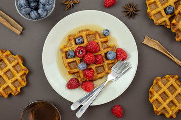 Belgian, carrot waffles with maple syrup and fresh raspberries, blueberry, cinnamon and star anise . Dark background. Top view. 