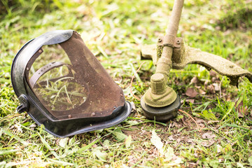 Gasoline mower and protective face mask on green meadow.